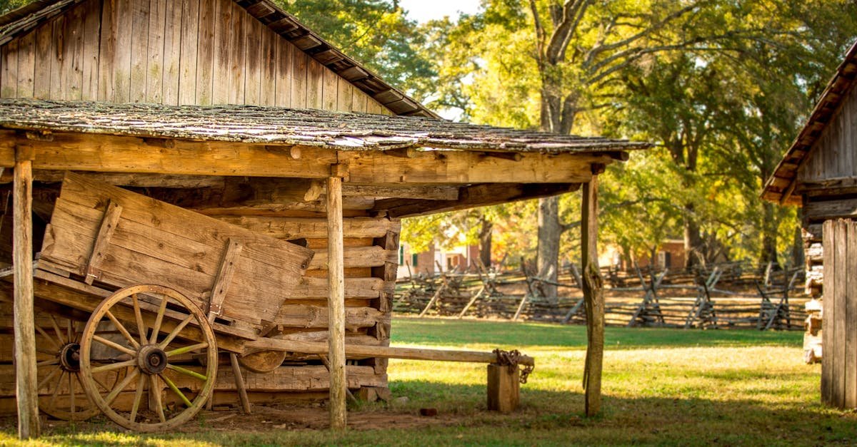 A rustic wooden barn with an old wooden wagon in a sunny outdoor farm setting.
