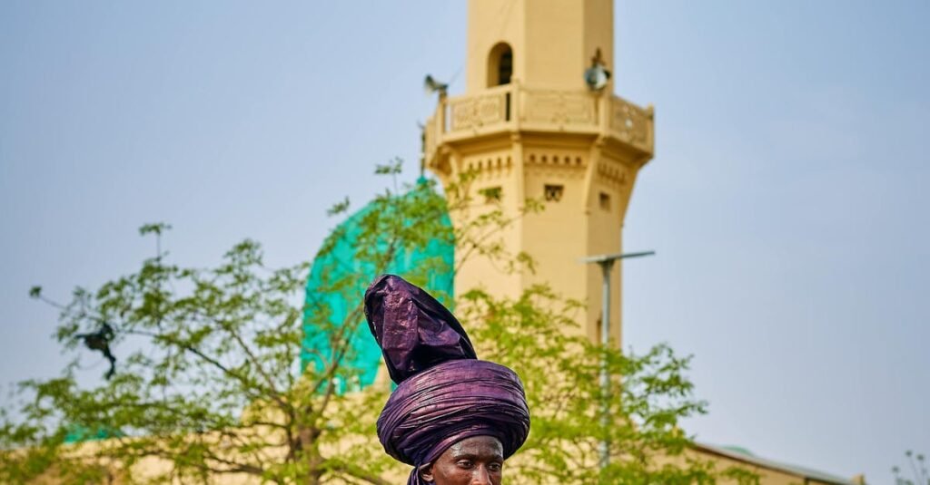 Vibrant traditional horse riders in colorful attire near a mosque tower in Nigeria.