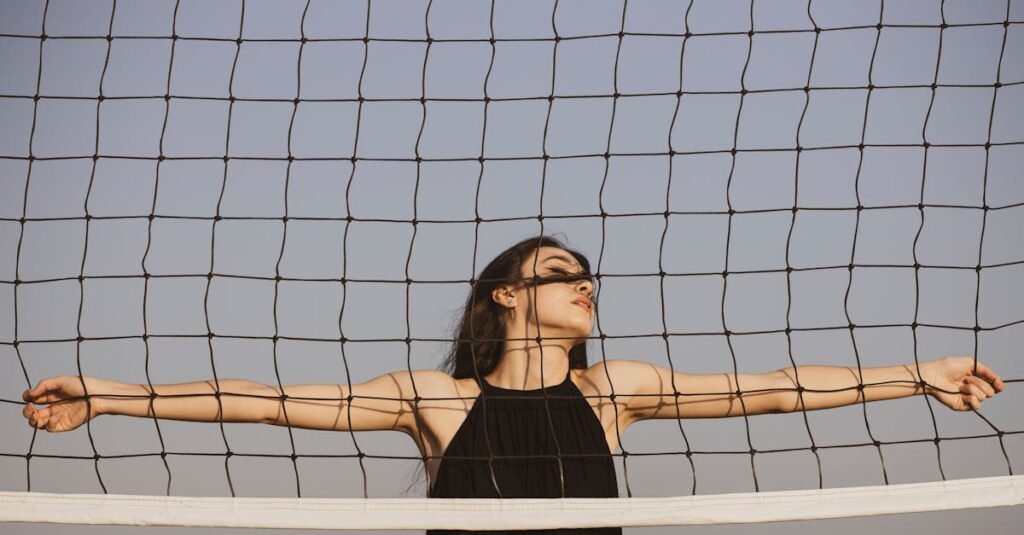 pexels-photo-3231040-3231040 Stylish woman in black dress poses gracefully behind a volleyball net under the clear blue sky.