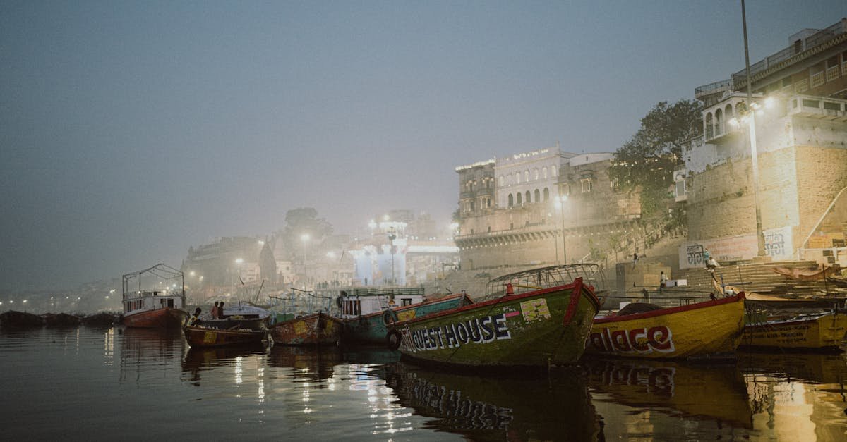 Misty evening view at Varanasi Ghats with colorful boats and illuminated buildings.