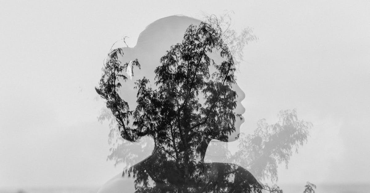 Artistic double exposure capturing a woman's silhouette blending with natural tree branches in black and white.
