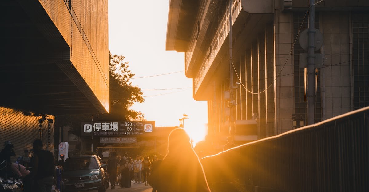 Person walking at sunset between buildings, capturing urban life and warm light in a bustling cityscape.
