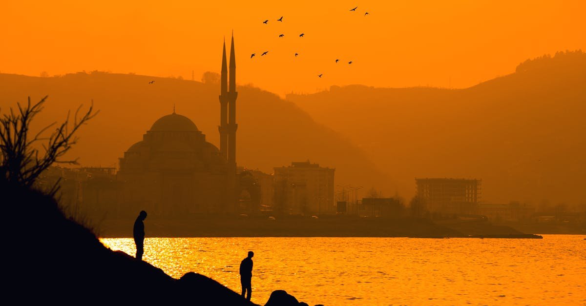 Silhouetted figures and mosque with birds at a vibrant Korgan sunset.