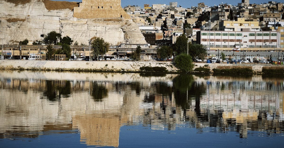 Captured reflection of an ancient fortress and city along a serene water body under a clear sky.