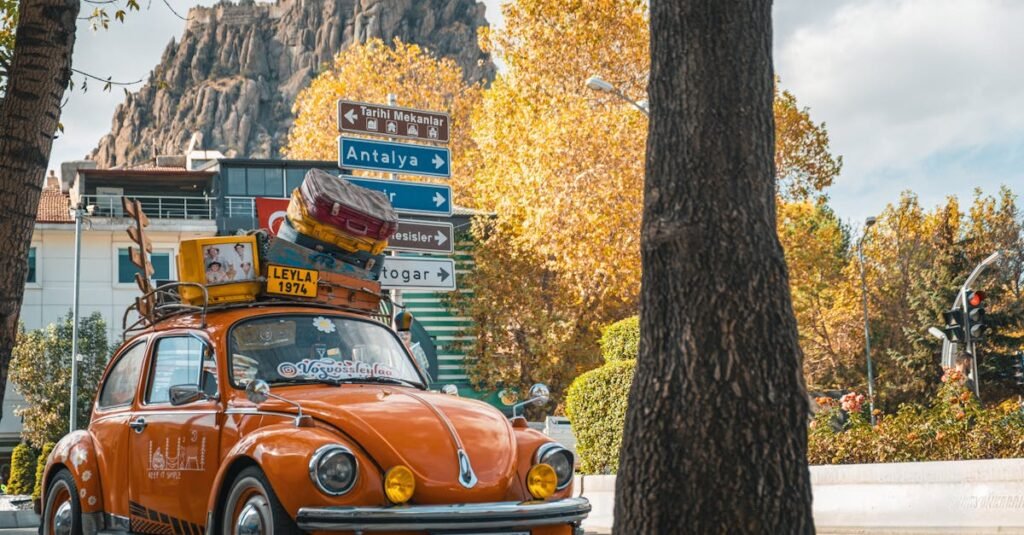 Classic orange Volkswagen Beetle with luggage, parked in Afyonkarahisar, Türkiye under autumn leaves.