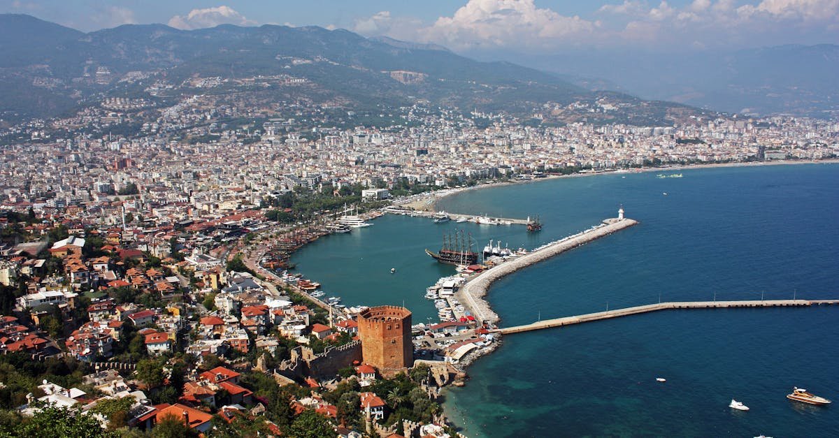 Aerial view of Antalya's harbor and cityscape with clear blue sea and historic sites.