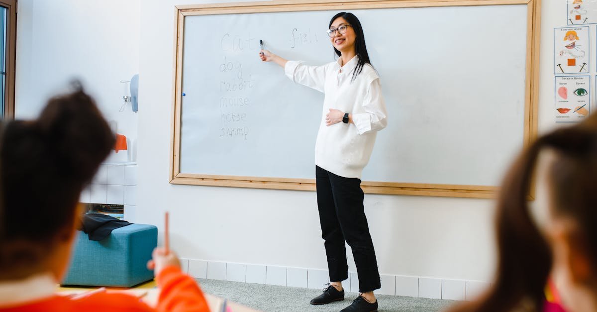 Smiling teacher instructing students in a classroom setting using a whiteboard.
