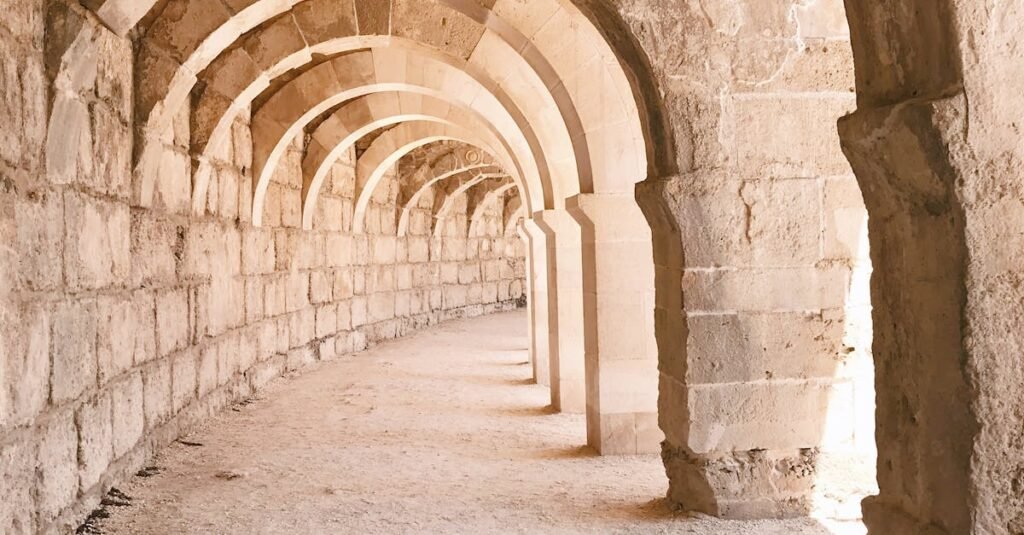 Old shabby stone construction with arched empty passage and sandy ground on street on sunny summer day