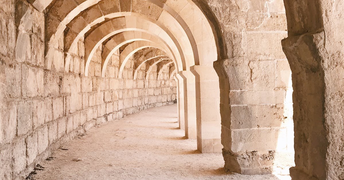 Old shabby stone construction with arched empty passage and sandy ground on street on sunny summer day