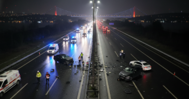 A dramatic high-angle nighttime shot of a highway accident scene in Istanbul. Emergency blue and red lights from police cars and ambulances reflect on the dark asphalt. Two damaged sedans are positioned in the emergency lane with scattered debris. Cinematic lighting, photorealistic style, 8k resolution, professional mood.
