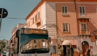 A public bus drives down a sunny street lined with colorful buildings.