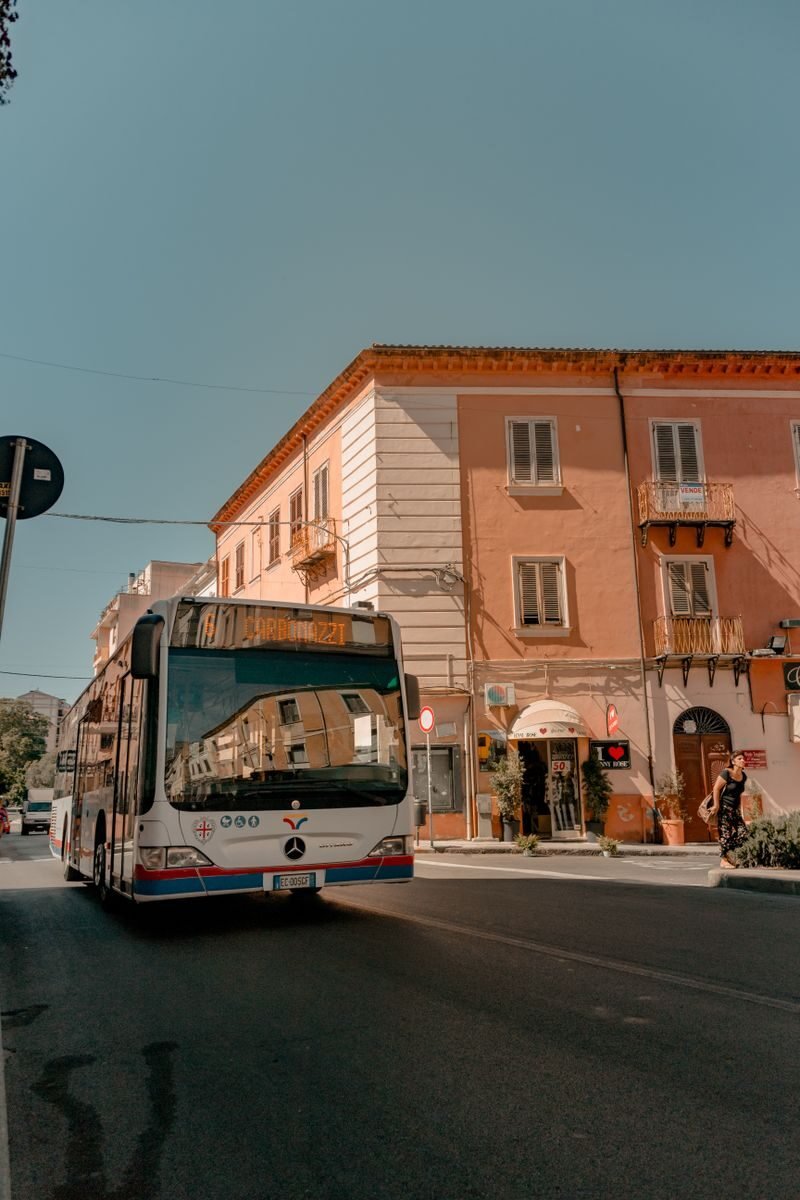 A public bus drives down a sunny street lined with colorful buildings.