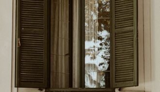 An artistic shot of a vintage wooden window with open shutters reflecting the outside view.