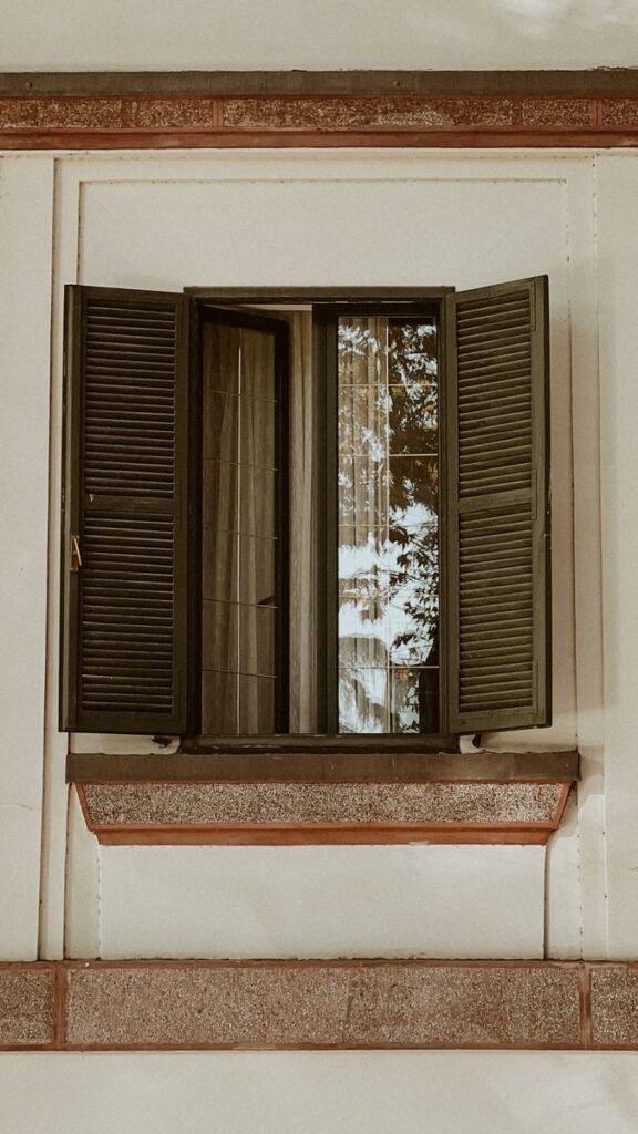 An artistic shot of a vintage wooden window with open shutters reflecting the outside view.