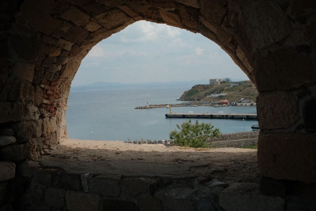 A scenic view of Bozcaada harbor through a stone archway, showcasing the island's historic charm.