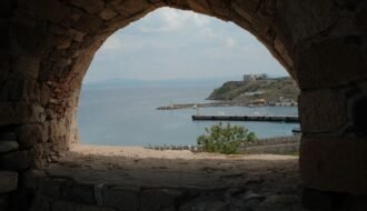 A scenic view of Bozcaada harbor through a stone archway, showcasing the island's historic charm.