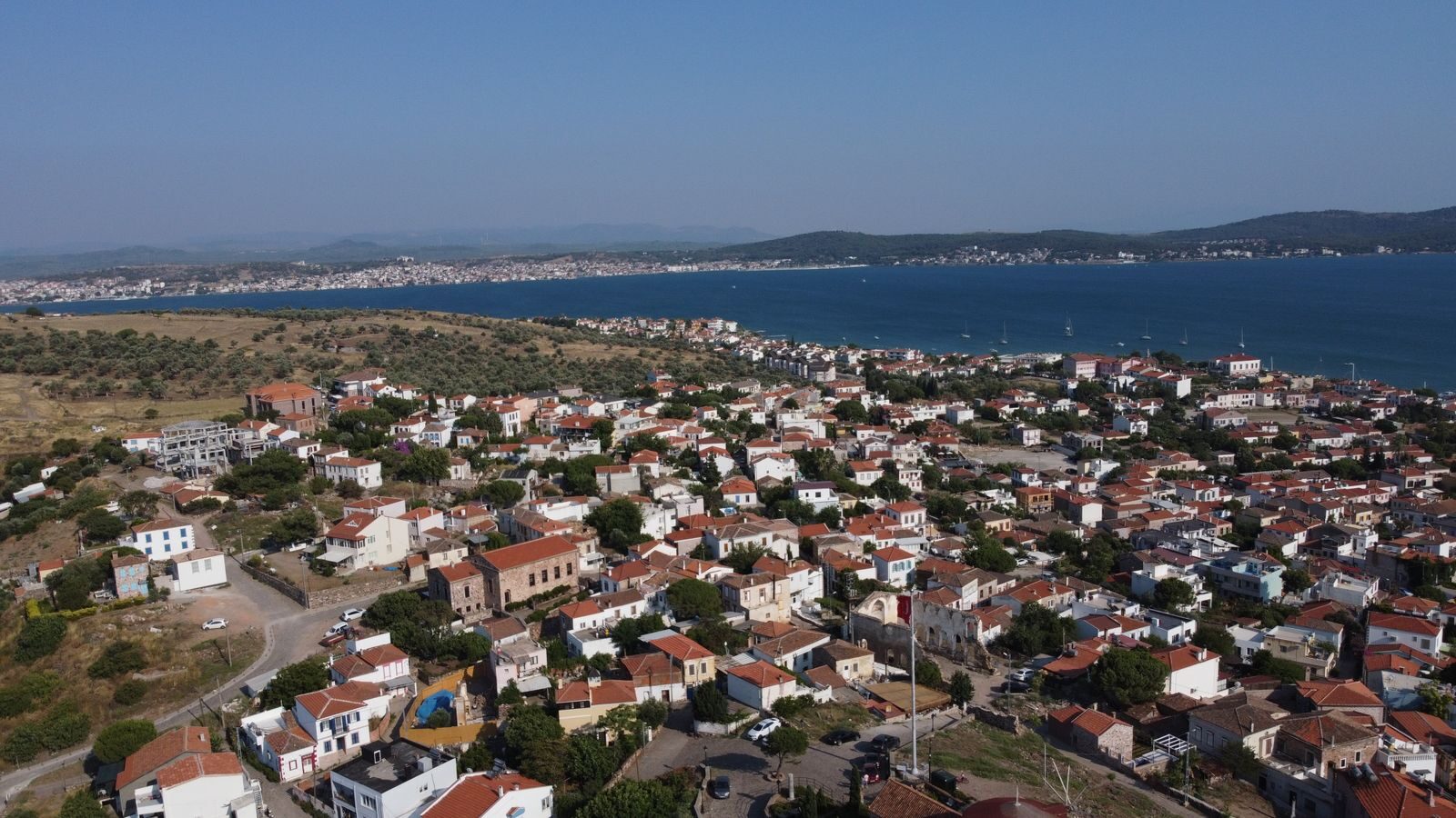 Aerial shot of Ayvalık's charming houses and coastline under a clear blue sky in summer.
