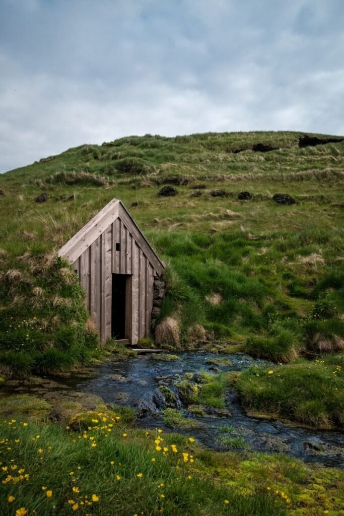 A traditional Icelandic turf house surrounded by lush greenery and a gentle stream.