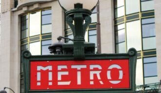 Close-up of the iconic Metro sign with an urban building backdrop in Paris.