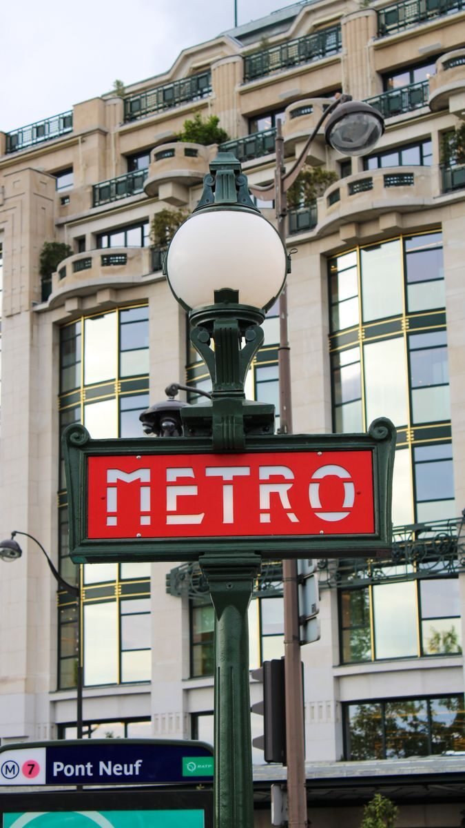 Close-up of the iconic Metro sign with an urban building backdrop in Paris.
