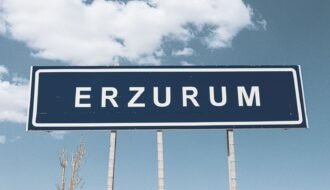 Street sign for Erzurum against a backdrop of a bright blue sky and fluffy clouds.