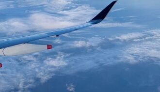View of clouds and distant land from an airplane, showcasing the beauty of aerial travel.