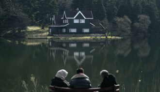 Peaceful scene of people sitting by a serene lake with a house and forest reflection in Bolu, Türkiye.