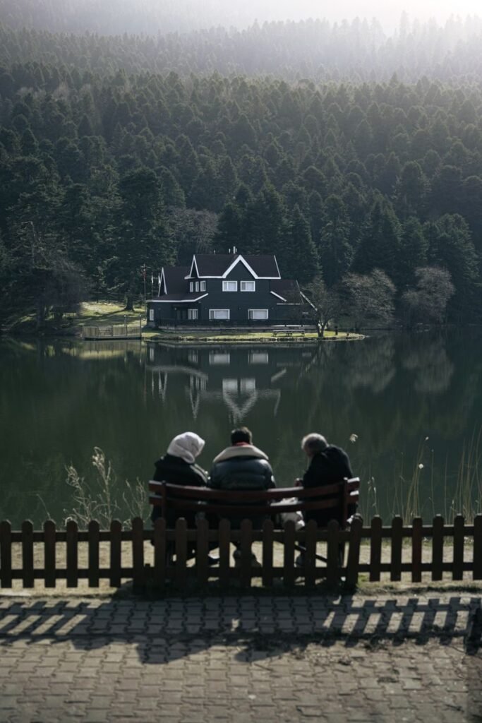Peaceful scene of people sitting by a serene lake with a house and forest reflection in Bolu, Türkiye.