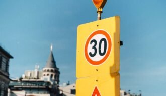 Yellow traffic sign displaying 30 speed limit with cityscape backdrop.