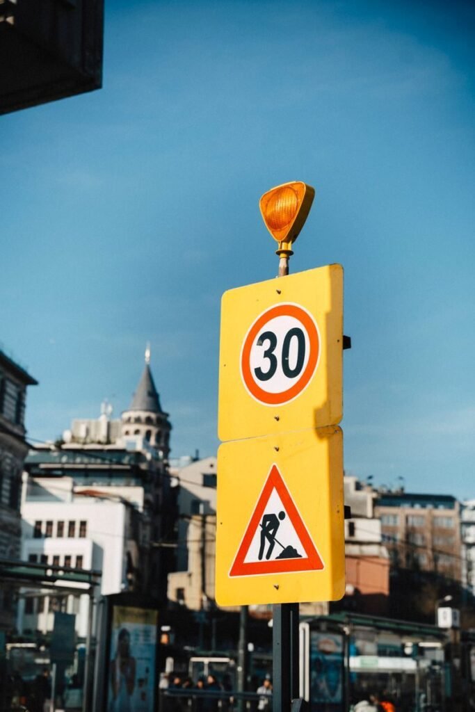 Yellow traffic sign displaying 30 speed limit with cityscape backdrop.