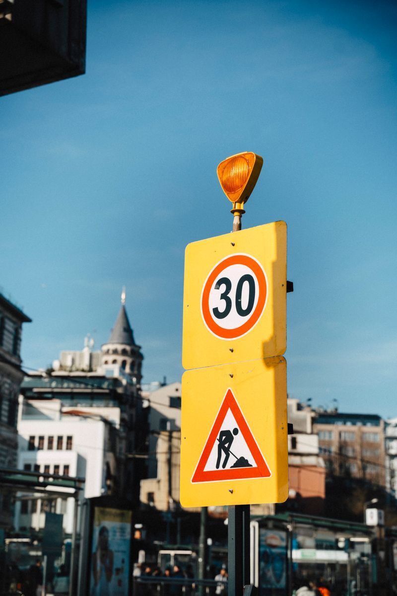 Yellow traffic sign displaying 30 speed limit with cityscape backdrop.