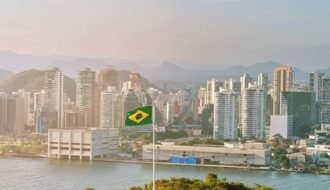 Aerial view of Brazilian flag atop green hill with city skyline in the background.