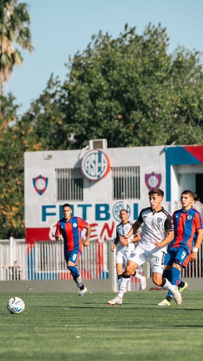 Soccer players in action during a game at Futbol Arena under bright daylight.