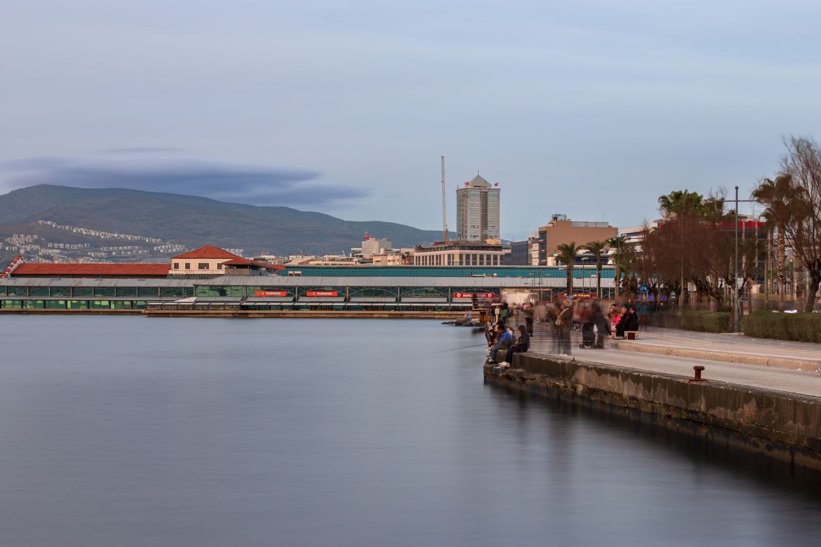 A tranquil evening at İzmir waterfront with distant cityscape and smooth water.