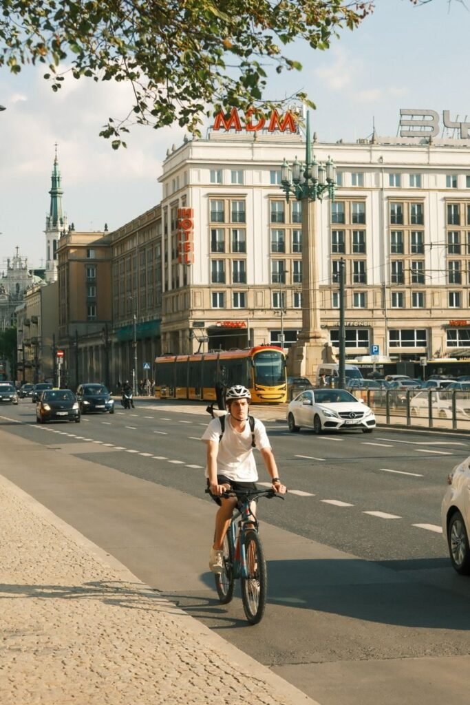 A cyclist rides through bustling Warsaw streets, showcasing urban life on a sunny day.