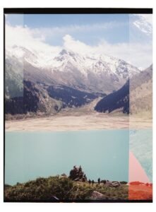 Turquoise lake, snowy mountains, and people on a rocky outcrop.