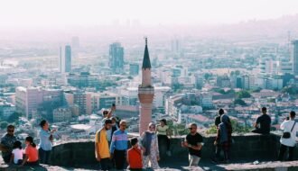 Tourists explore a historic site in Ankara with a panoramic city view, capturing blend of heritage and urban life.