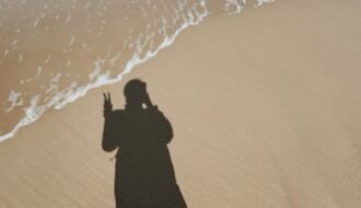 Shadow of a person on a sandy beach with waves.
