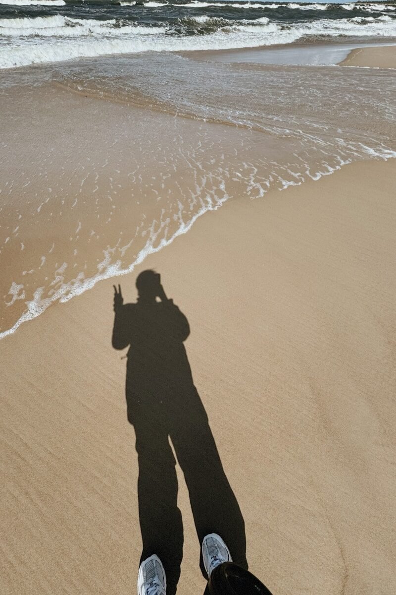 Shadow of a person on a sandy beach with waves.