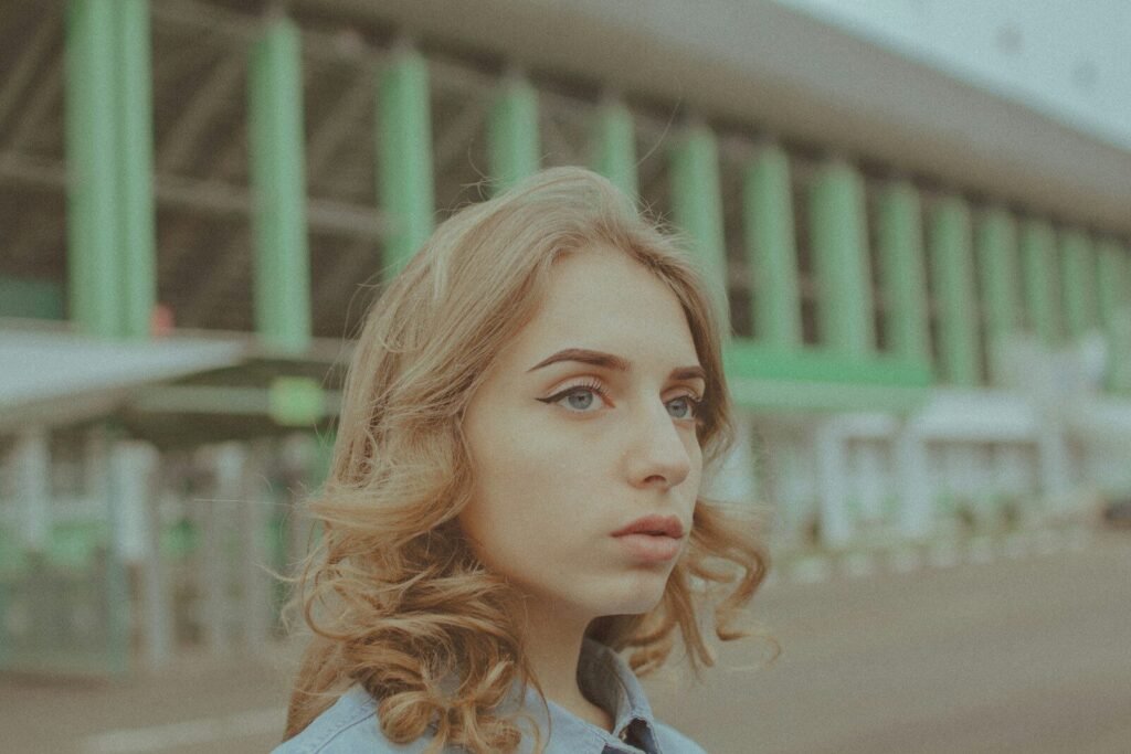 Young woman with wavy hair looking away, green building background.