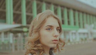 Young woman with wavy hair looking away, green building background.