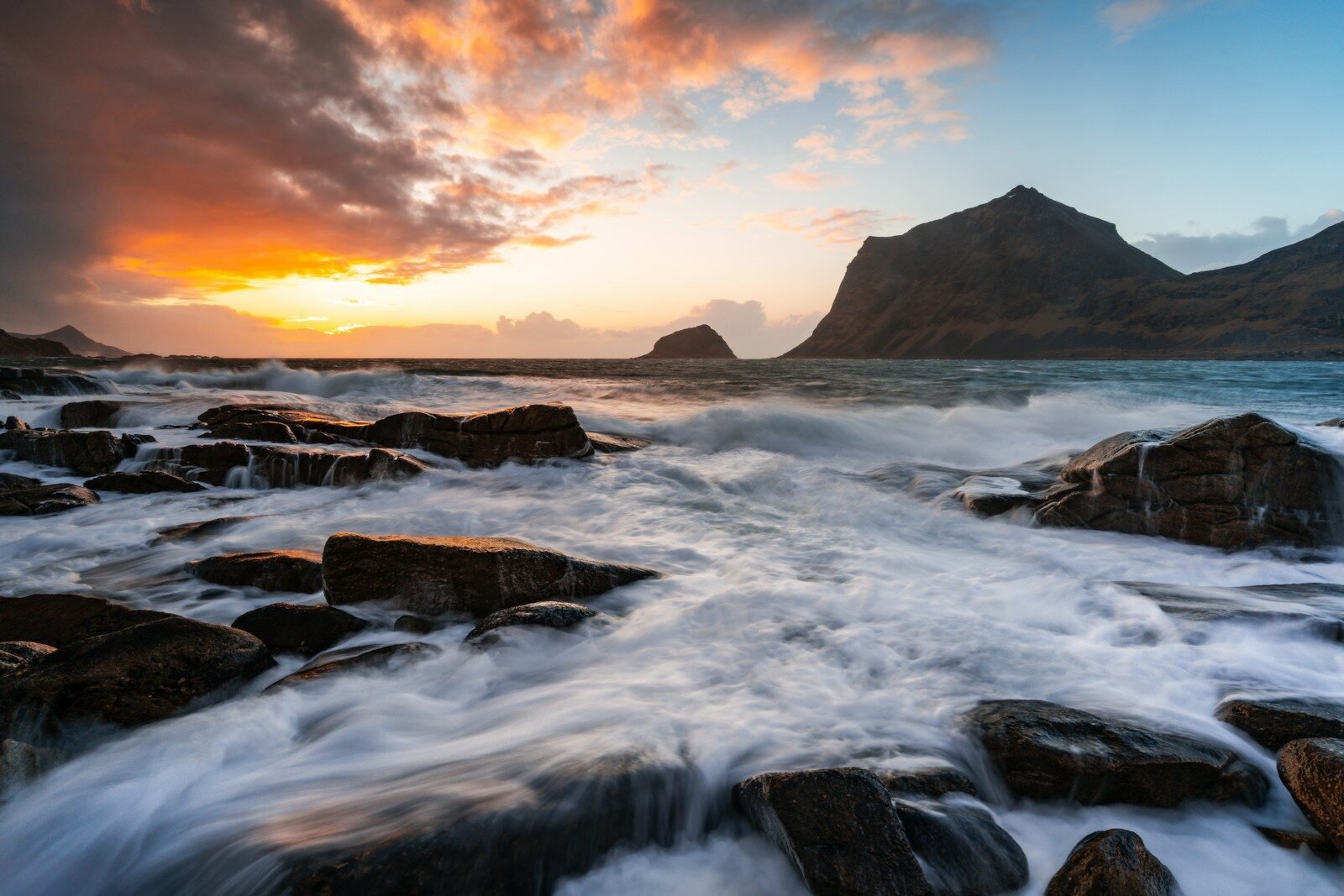 Vibrant sunset illuminates ocean waves crashing on a rocky shore.