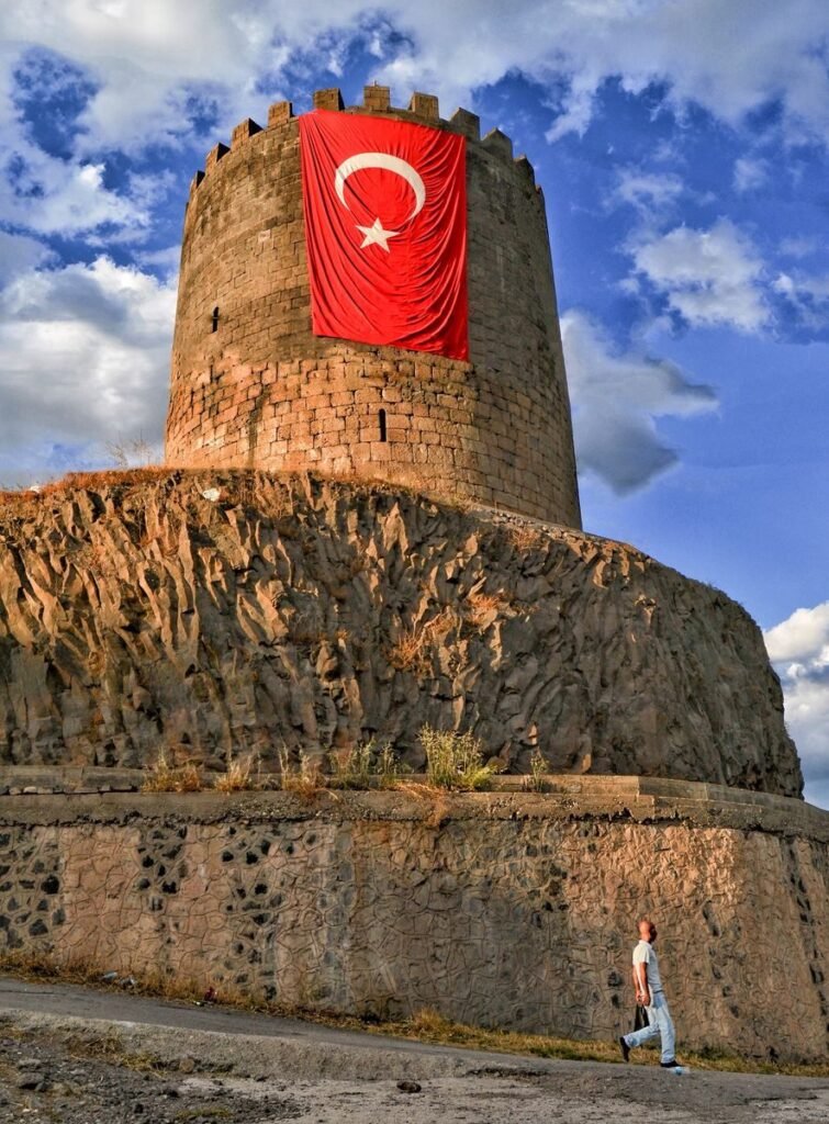 Medieval tower in Diyarbakır, Türkiye with a Turkish flag under a vibrant blue sky.