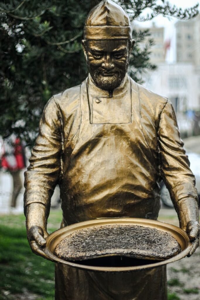 Bronze statue of a chef holding Hatay's traditional dish outdoors in Türkiye.