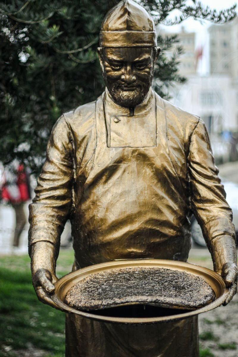 Bronze statue of a chef holding Hatay's traditional dish outdoors in Türkiye.