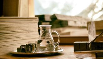 A peaceful still life scene with a glass water pitcher and books on a wooden table by the window.