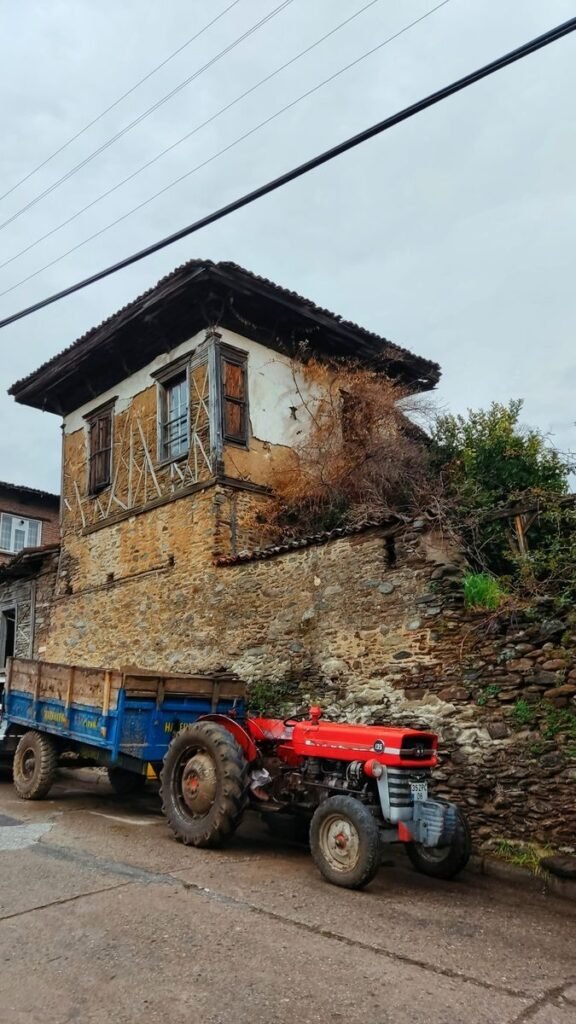 A vintage red tractor parked beside an old stone house with wooden shutters.