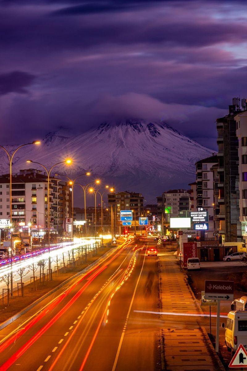 Busy city street lit at night with distant mountain view in Aksaray, Türkiye.