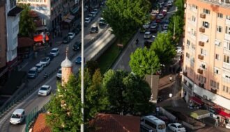 Aerial view of a bustling city roundabout filled with traffic, surrounded by tall buildings and vibrant greenery.