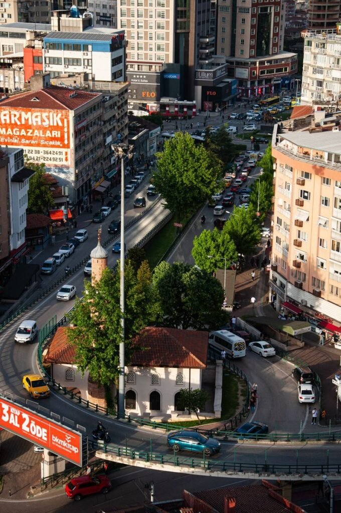 Aerial view of a bustling city roundabout filled with traffic, surrounded by tall buildings and vibrant greenery.